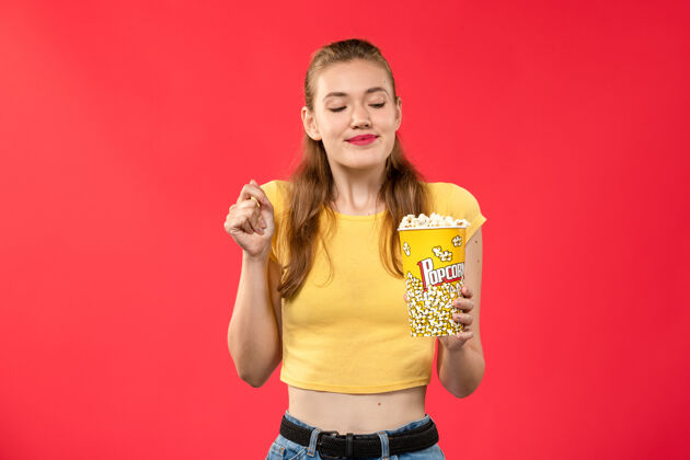 观点正面图年轻女子在电影院拿着爆米花上了红墙电影院的女彩漂亮电影电影院
