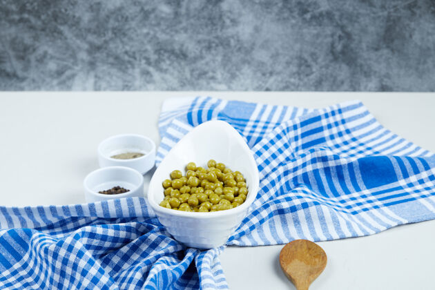 桌布在一张白色的桌子上放一个白色的碗里煮青豌豆 上面放着香料 勺子和桌布煮熟烹饪烹饪