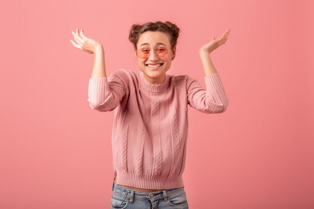 情感年轻漂亮活泼的笑脸女郎 穿着粉色毛衣 戴着春日流行的太阳镜 以粉色工作室为背景粉色微笑傻瓜