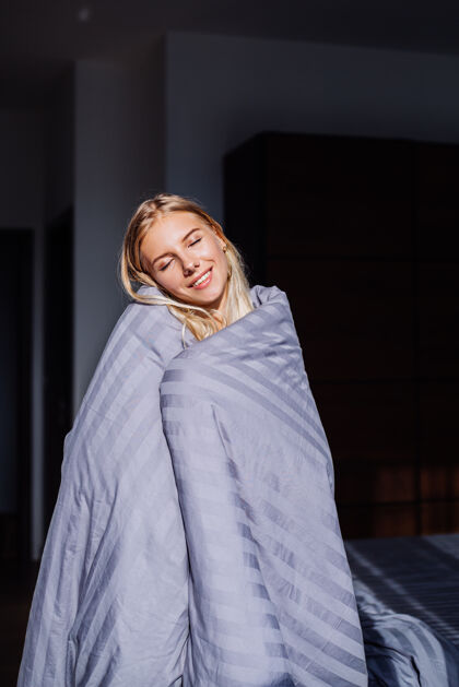 快乐卧室里的快乐平静的女人肖像 穿着灰色的条子毯子和黑米色的身体 在家睡觉穿漂亮舒适女人
