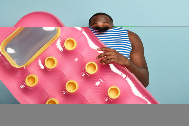 个性脸色黝黑的男性度假者手持粉色充气床垫 准备游泳 欢笑不已放松乐观充气