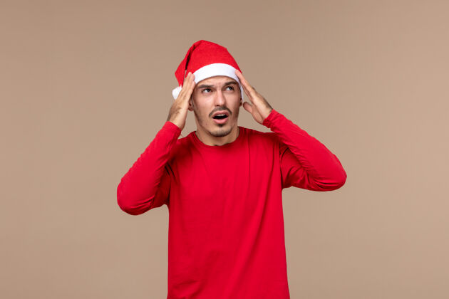 背景正面图棕色背景上表情混乱的年轻男性圣诞假期感慨一服装年轻