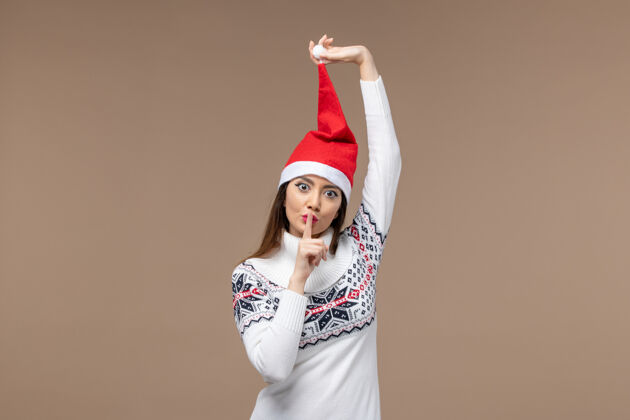 快乐正面图：棕色背景上戴着红色圣诞帽的年轻女性圣诞假期感慨情感黑发微笑