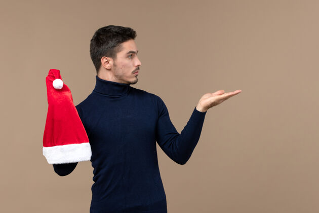 视图正面图：年轻男子在棕色背景圣诞假期玩红帽子前面年轻年轻男性