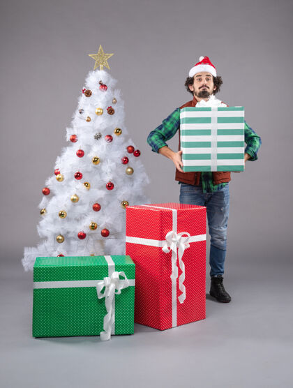 灰色年轻的男性在灰色的节日礼物包圣诞树圣诞老人