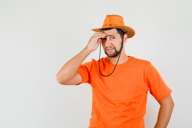 休闲年轻人穿着橙色t恤 戴着帽子 揉着额头 看上去很悲伤前视图男性模特成人