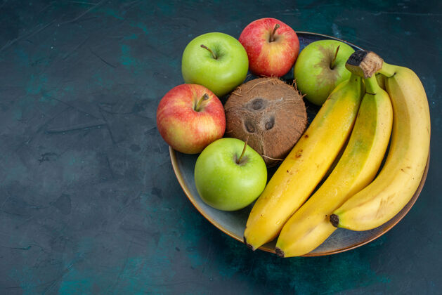 热带前视不同水果组成椰子苹果和香蕉深蓝色桌上水果新鲜醇香异国情调热带苹果椰子可食用