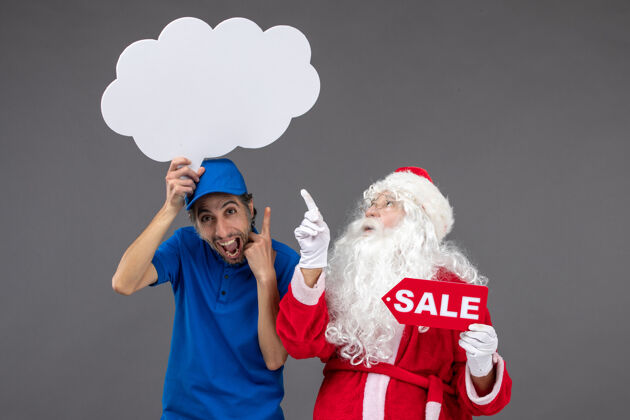 快乐圣诞老人的正面图 男信使手持白云招牌 在灰色墙上出售人服装圣诞快乐