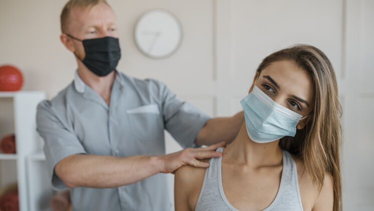 面罩男理疗师在与女患者进行治疗时戴着医用面罩治疗初级理疗