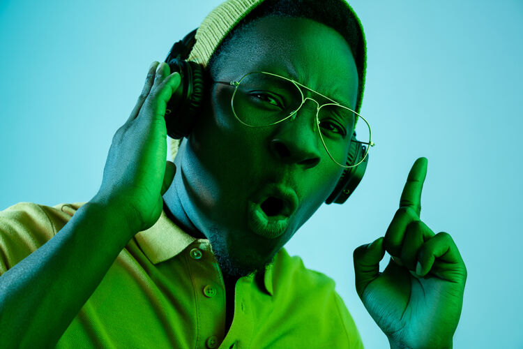 夜总会年轻帅气的快乐惊喜的时髦男人在霓虹灯下用耳机听音乐迪斯科舞厅 夜总会 嘻哈风格 积极的情绪 面部表情 舞蹈概念人物音乐非洲