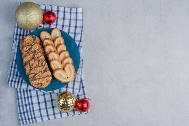 片状一排排饼干放在蓝色的木板上 旁边是放在大理石表面毛巾上的圣诞饰品美味糖毛巾
