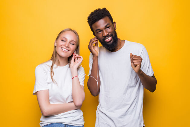 休闲一对快乐的夫妇一边唱歌 一边用智能手机和耳机隔着黄色的墙一起唱歌人惊人耳机