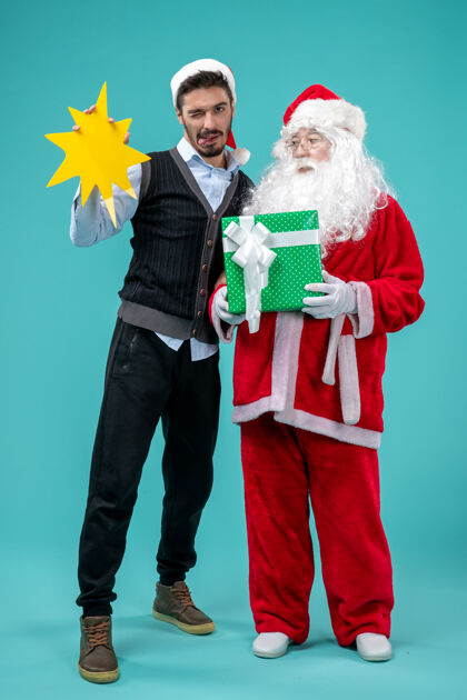 蓝色前视图：圣诞老人和手持蓝色背景黄色标志的年轻男性举行圣诞老人圣诞老人