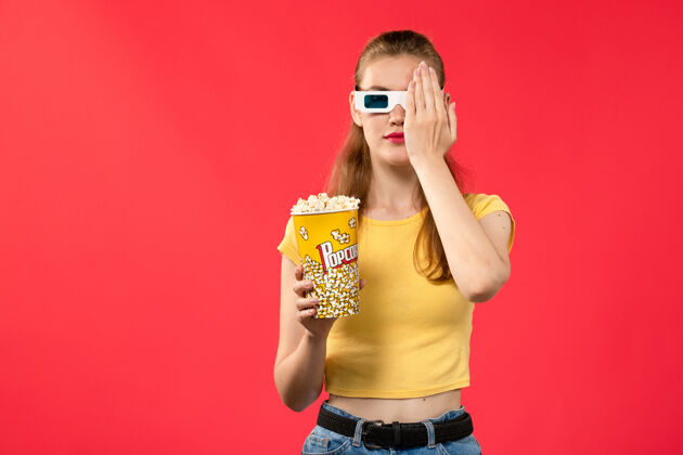 漂亮前视图年轻女性在电影院拿着爆米花包在红墙电影院的d太阳镜电影电影身体