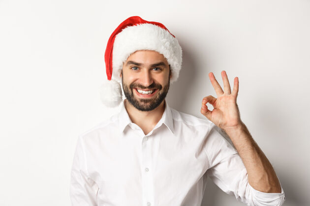 推荐派对 寒假和庆祝的概念自信的男子在圣诞帽显示好的标志 批准和喜欢圣诞节商人胡须