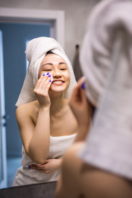 皮肤美丽的亚洲女人光着皮肤 穿着白色浴袍 在清晨清新的阳光下洗脸 呵护清洁面部头部健康皮肤护理