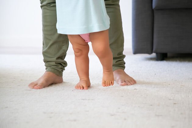 赤脚赤脚婴儿的腿试图走在妈妈面前孩子在妈妈的支持下迈出了第一步不规则的镜头为人父母和童年的概念婴儿裁剪走路