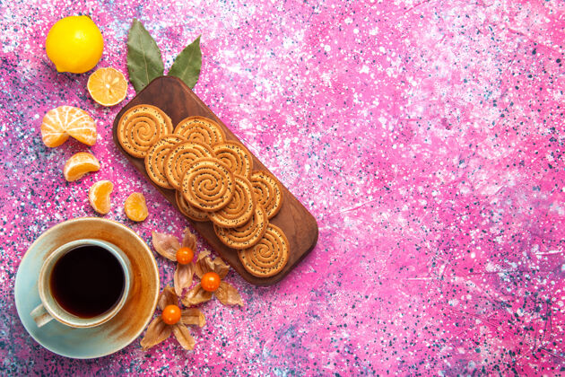 糖果在粉红色的表面上有一杯茶和柑橘的甜饼干俯视图柑橘茶饼干