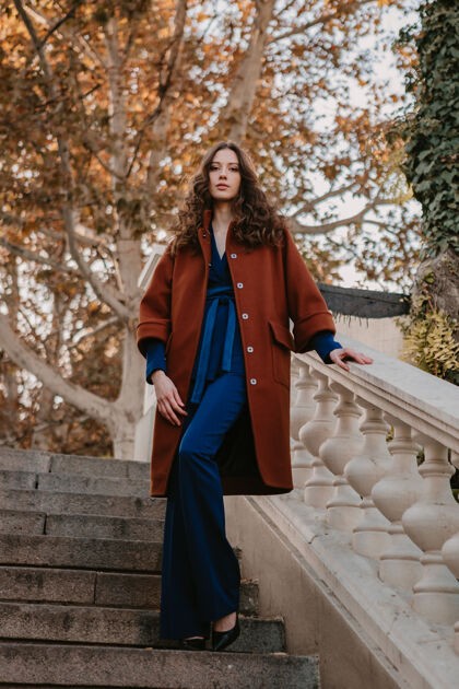 户外美丽时尚的微笑瘦身女子卷发走在街头楼梯上穿着温暖的棕色外套和蓝色西装 秋季时尚街头风优雅欢快深色