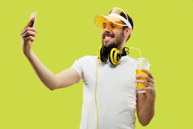 惊喜穿着衬衫的年轻人的肖像戴着耳机和饮料的男模人类的情感 面部表情 夏天 周末的概念自拍饮料乐趣男性