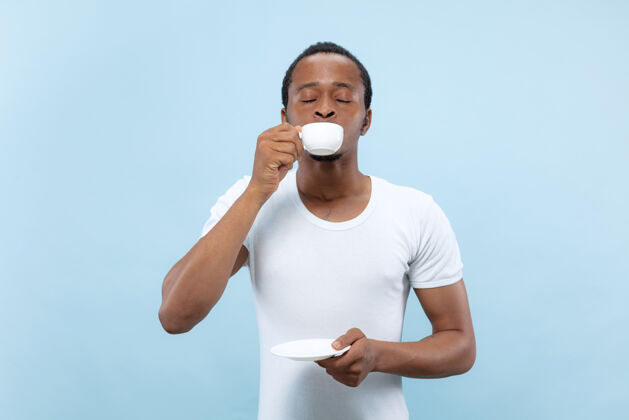 非洲人穿着白衬衫的非洲裔美国年轻人的特写肖像享受 喝咖啡 微笑快乐男性咖啡