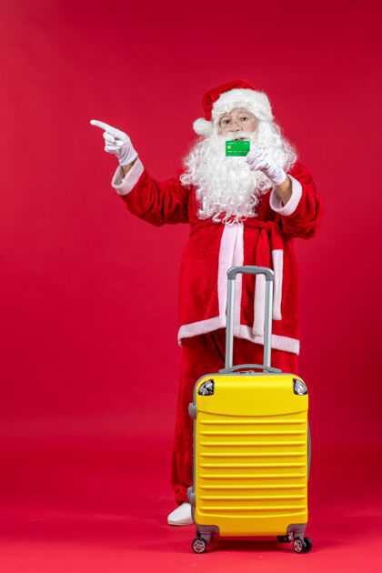 圣诞老人红墙上挂着黄色袋子 手里拿着绿色银行卡的圣诞老人的正视图人人们节日