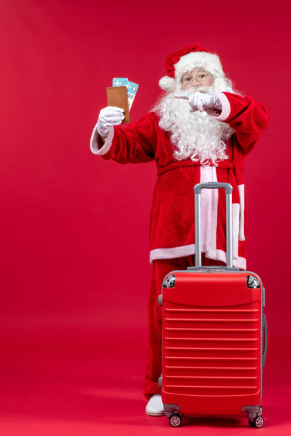 圣诞快乐圣诞老人的前视图 带着包 拿着票 准备在红墙上旅行前面圣诞老人圣诞老人