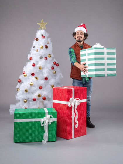 时尚年轻的男性在灰色的圣诞礼物周围礼物圣诞帽圣诞