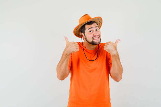 手势穿着橙色t恤 戴着帽子 兴高采烈地朝前看的年轻人竖起了大拇指衬衫工作室男性