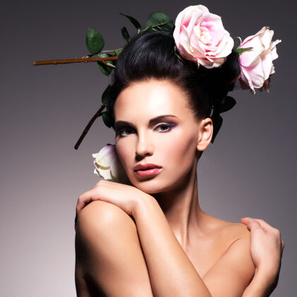 手美丽的年轻女子的肖像与鲜花在头发的姿势发型深色花