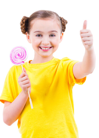 饮食穿黄色t恤的快乐漂亮女孩 彩色糖果 竖起大拇指-白色隔离糖果小衬衫