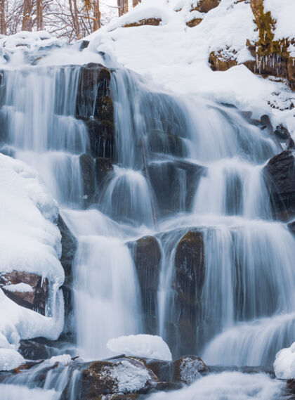 砾石冰水的小山瀑在白雪覆盖的湿石头间流动鹅卵石瀑布雨