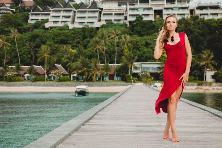 连衣裙年轻漂亮迷人的女人独自站在豪华度假酒店的码头上 暑假 红色长裙 金色头发 性感服装 热带沙滩 诱惑 性感 微笑时尚礼服奢华