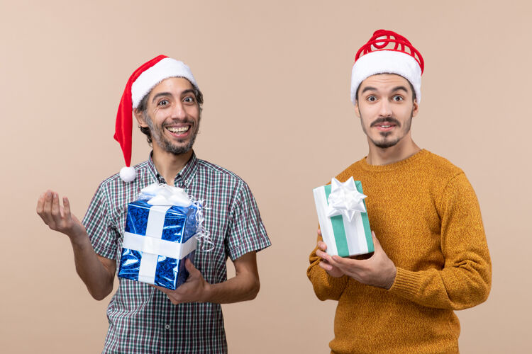 两个微笑的男人正面图两个微笑的家伙戴着圣诞帽 拿着圣诞礼物 背景是米色的礼物风景帽子