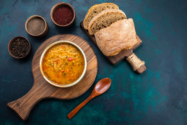 面包在深蓝色的桌子上 用面包和调味品放在圆盘子里 俯瞰美味的蔬菜汤汤美味香料