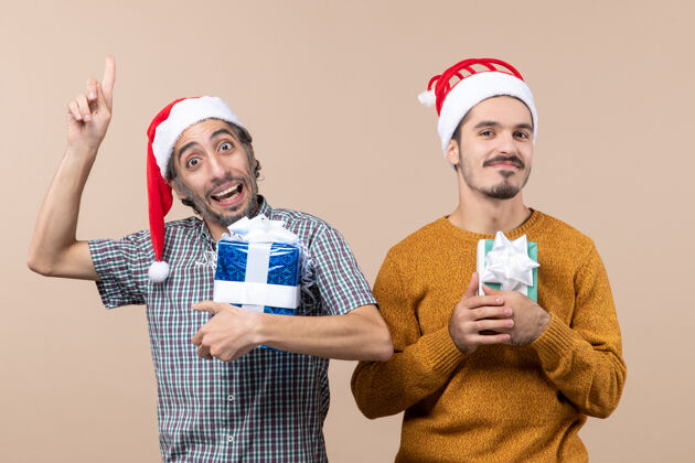 视图正面图两个满意的家伙拿着圣诞礼物和一个显示在米色孤立的背景上面的东西礼物成人显示