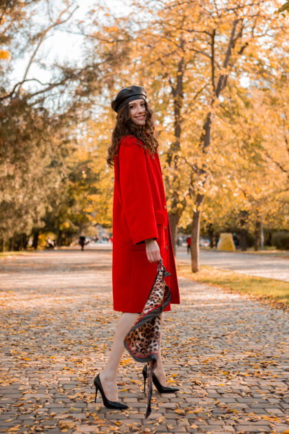 休闲迷人时尚微笑的女人卷发漫步在公园穿着暖红色外套秋季时尚 街头风格 戴贝雷帽和豹纹围巾女士穿着户外