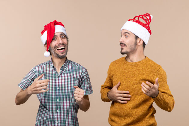 伙计们正面图两个戴着圣诞帽的快乐的家伙在米色孤立的背景下大笑大笑男帽子