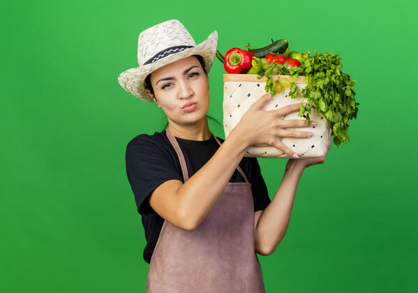 漂亮年轻漂亮的女园丁围着围裙 戴着帽子 手里拿着装满蔬菜的箱子 表情严肃围裙严肃的蔬菜