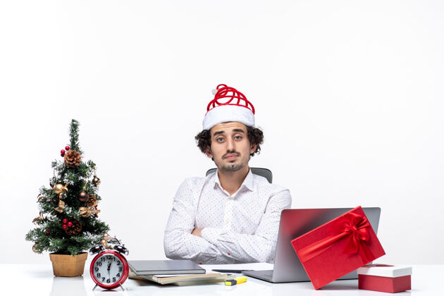 圣诞老人在白色背景的办公室里 戴着滑稽的圣诞老人帽子的年轻商人在镜头前摆出一副惊讶而疲惫的姿势卖家年轻人