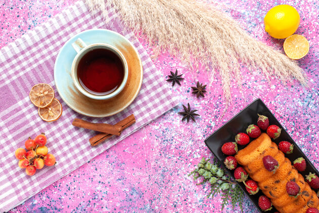 烘焙在粉红色的桌子上可以看到美味的蛋糕和新鲜的红色草莓和茶饮料饼干红色