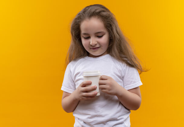 抱着微笑的小女孩穿着白色t恤 在孤立的橙色背景上拿着一杯咖啡小橙色咖啡