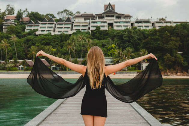 赤脚穿着黑色连衣裙的美丽迷人的女人在豪华度假酒店的码头上摆姿势 暑假 热带海滩放松放松大海