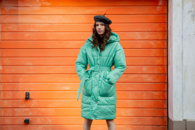服装穿着冬秋时尚潮流蓬松外套和帽子贝雷帽的时髦女人在街上对着橙色的墙壁摆姿势女人街头风格女人