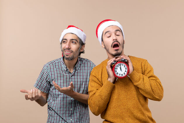 闭着的前视图两个圣诞老人一个拿着闹钟 眼睛闭着 背景是米色的微笑两个圣诞男人男人