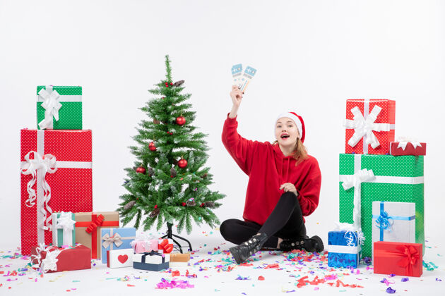 圣诞快乐前视图年轻女子坐在一个白色的墙上拿着飞机票的礼物人旅行圣诞节