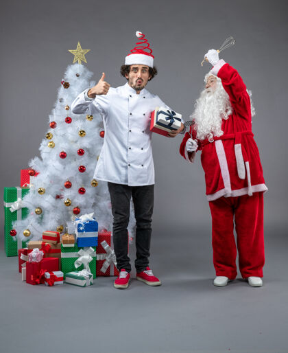 圣诞老人圣诞老人与男性厨师和圣诞礼物在灰色墙上的正面视图十二月礼物人