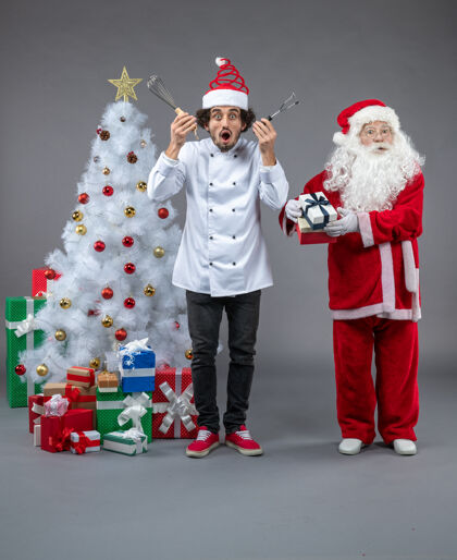 快乐圣诞老人和男厨师在灰色墙上围着圣诞礼物的正视图快乐前面十二月