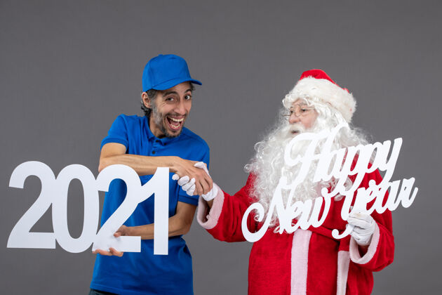 快乐圣诞老人与男信使举行和新年快乐和2021年板在灰色墙上的正面视图人圣诞快乐工人