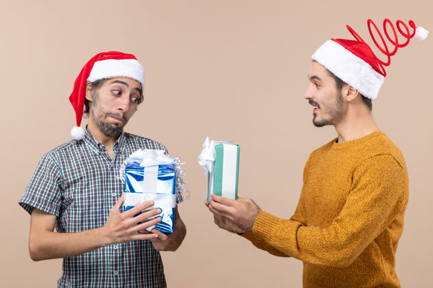 圣诞老人两个戴着圣诞帽的家伙在米色背景上交换圣诞礼物米色风景穿着